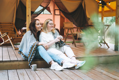 Two young women friends drinking tea and relaxing in glamping in the woods