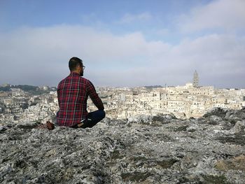 Rear view of man sitting on building against sky