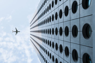 Airplane flying by building in city against sky