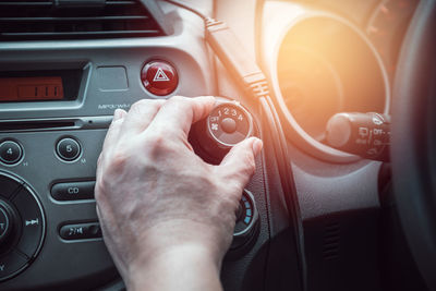 Cropped hand of man adjusting fan button in car