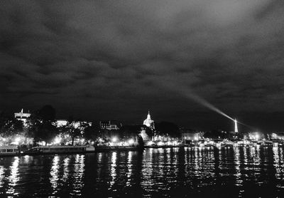 Illuminated city by river against sky at night