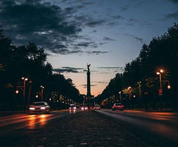 Cars on city street against sky at dusk