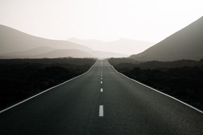 Diminishing perspective of empty road leading towards mountains against sky