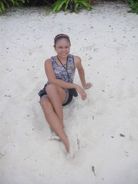 Portrait of smiling young woman sitting on sand at beach