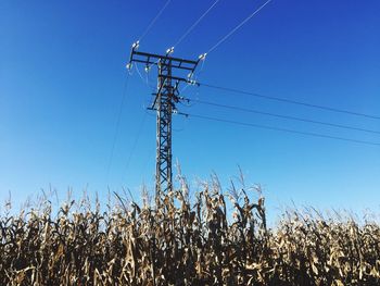 Low angle view of electricity pylon against clear blue sky
