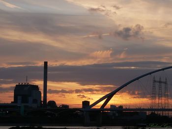 Silhouette factory against sky during sunset