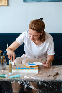 Woman artist painting picture at home with acrylic paints and spatula on online lesson via tablet