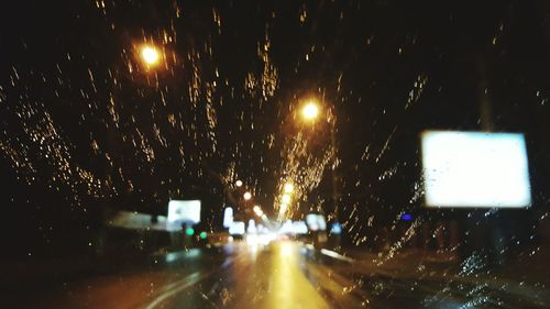 Illuminated road seen through wet windshield during rainy season