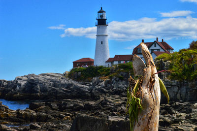 Lighthouse amidst rocks and buildings against sky