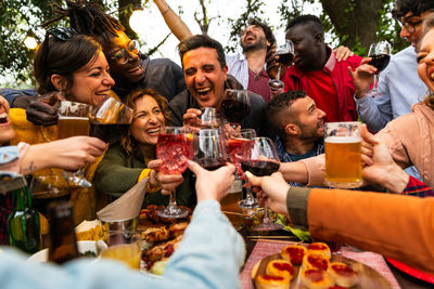 Group of people toasting with wine and beer - happy friends having fun outdoor