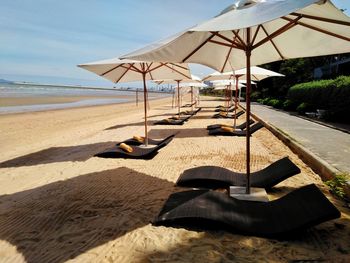 Lounge chairs and parasols on sand at beach against sky