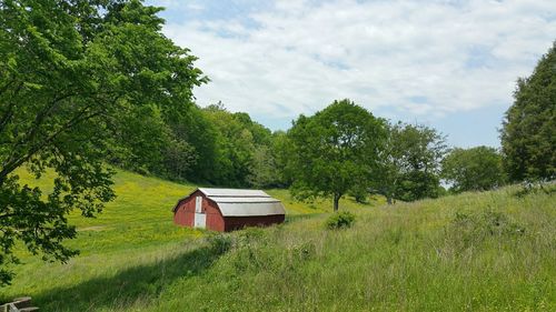 Red barn amidst trees on field against sky