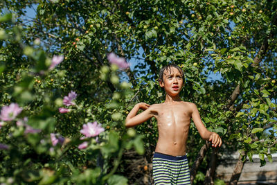 Shirtless boy standing against tree