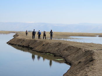 People standing by lake against clear sky