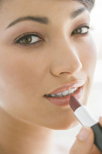 Close-up portrait of beautiful woman applying lipstick on lips