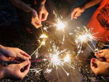 Cropped hands of friends holding illuminated sparklers on street at night