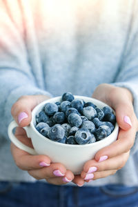 Woman holding bowl with frozen blueberry fruits. harvesting concept. female hands collecting berries