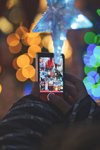 Cropped hand holding illuminated christmas tree at night