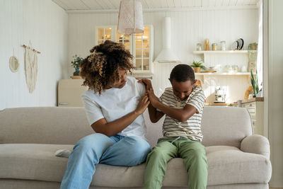 Side view of mother and daughter sitting on sofa at home