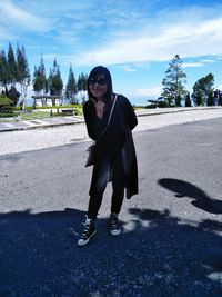 Portrait of smiling young woman standing on road against sky