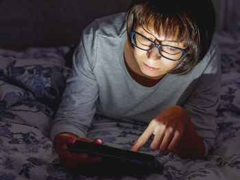 Midsection of boy using mobile phone on bed