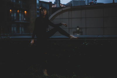 Woman sitting on retaining wall during dusk