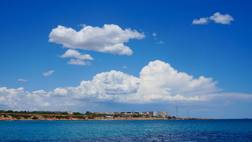 View to calm sea, blue sky, white clouds and coastline from water on sunny day