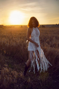 Fashion portrait of a curly-haired woman in white clothes stand on a field with dry grass in autumn