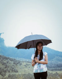 Young woman standing with umbrella in rain against sky