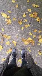 Low section of person standing on autumn leaves on road