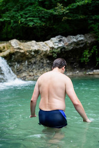 Tropical nature and vacation. back view of a well-built man swimming in the mountain river with 