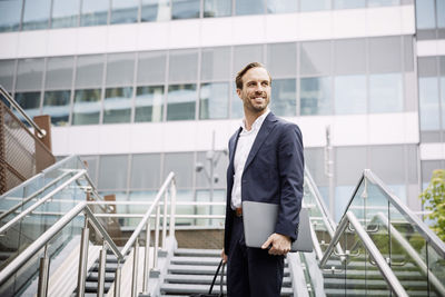 Low angle view of thoughtful male lawyer with laptop standing on steps