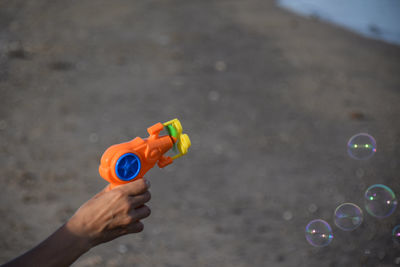 Close-up of hand holding bubble gun against  sand beach. 