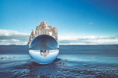 Close-up of crystal ball on beach against blue sky