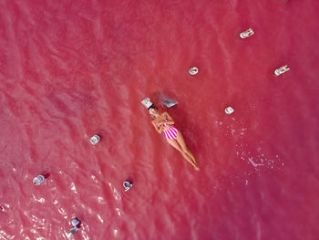 Woman in a pink bathing suit lies on a ruined wooden bridge in the middle of a pink lake in summer