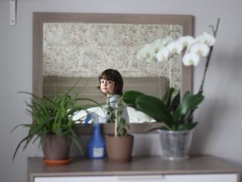 Mirror with reflection of boy sitting on bed at home