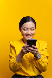 Smiling young man using smart phone against yellow background