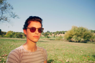 Portrait of young woman wearing sunglasses standing on field against clear sky