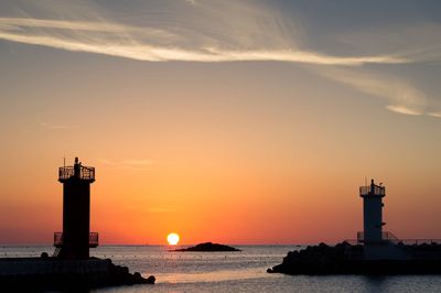 Lighthouse by sea against sky during sunset