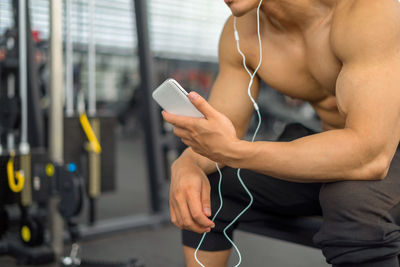 Midsection of shirtless muscular man using mobile phone in gym