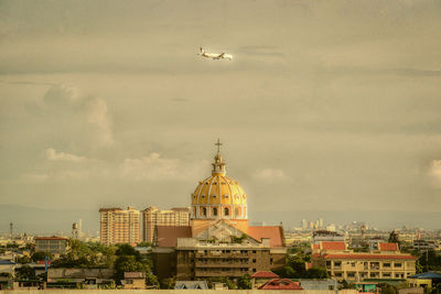 Airplane flying over buildings in city against sky