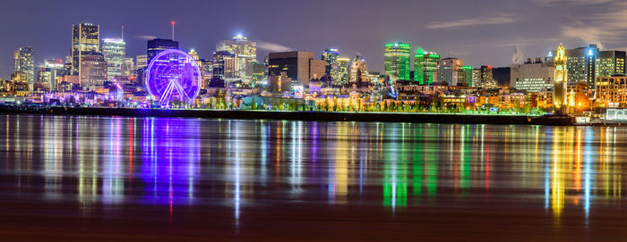 Illuminated buildings by river against sky at night