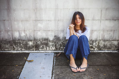 Full length of woman sitting on footpath