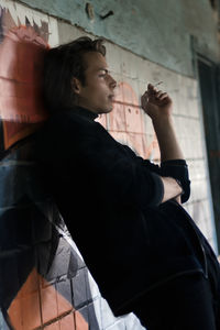 Side view of young man smoking cigarette by wall