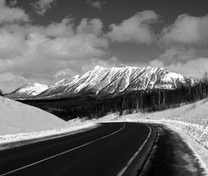 Empty road by snowcapped mountains against sky