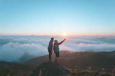 Male friends standing on rock against sky during sunset