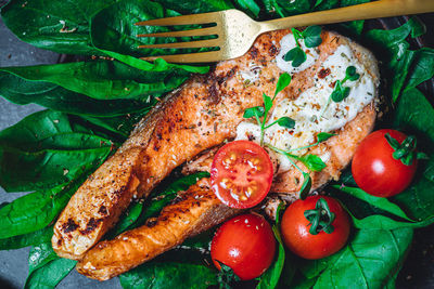 A plate with fresh green raw spinach and fried wild salmon, tomatoes and cream cheese sauce 