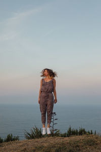 Full length of woman jumping while tossing hair against sea and sky during sunset