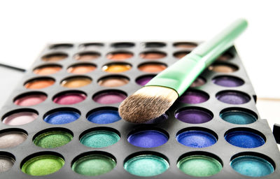 Close-up of multi colored beauty product with make-up brush against white background