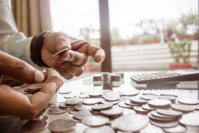 Cropped image of businessman counting coins using calculator at desk in office.